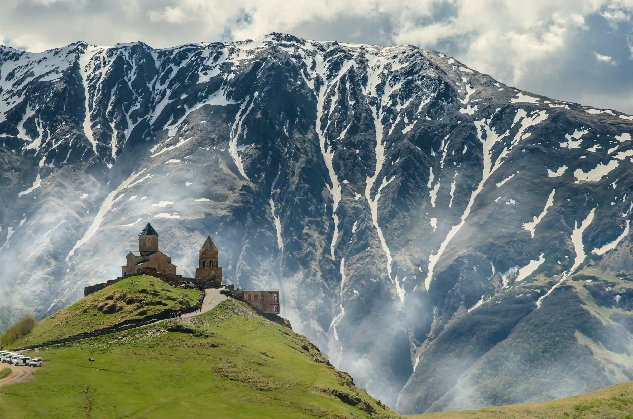 Gergeti Trinity Church on a green hill below the snow-capped Caucasus mountains, Georgia