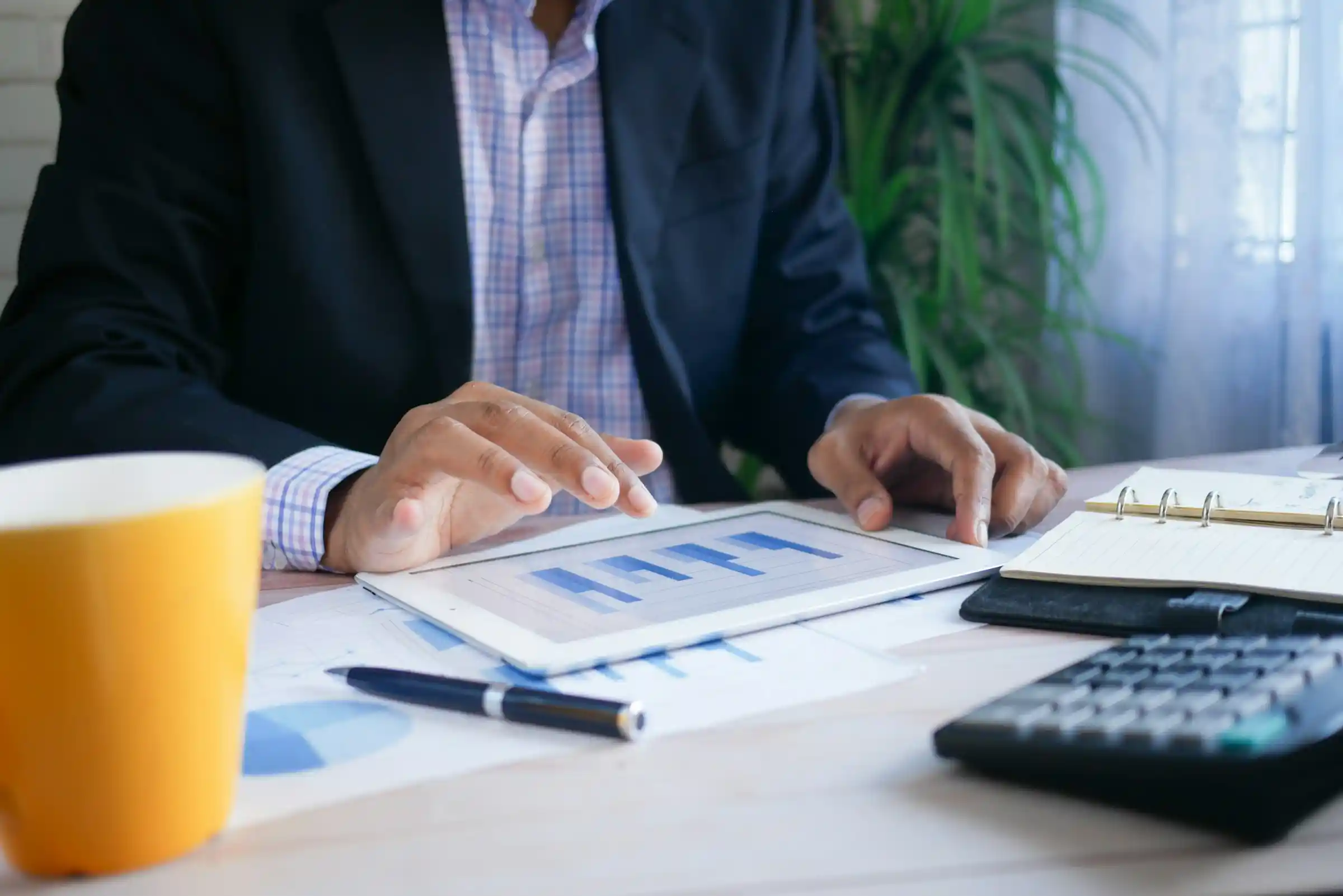 A person reviewing financial charts on a tablet with a calculator at a desk