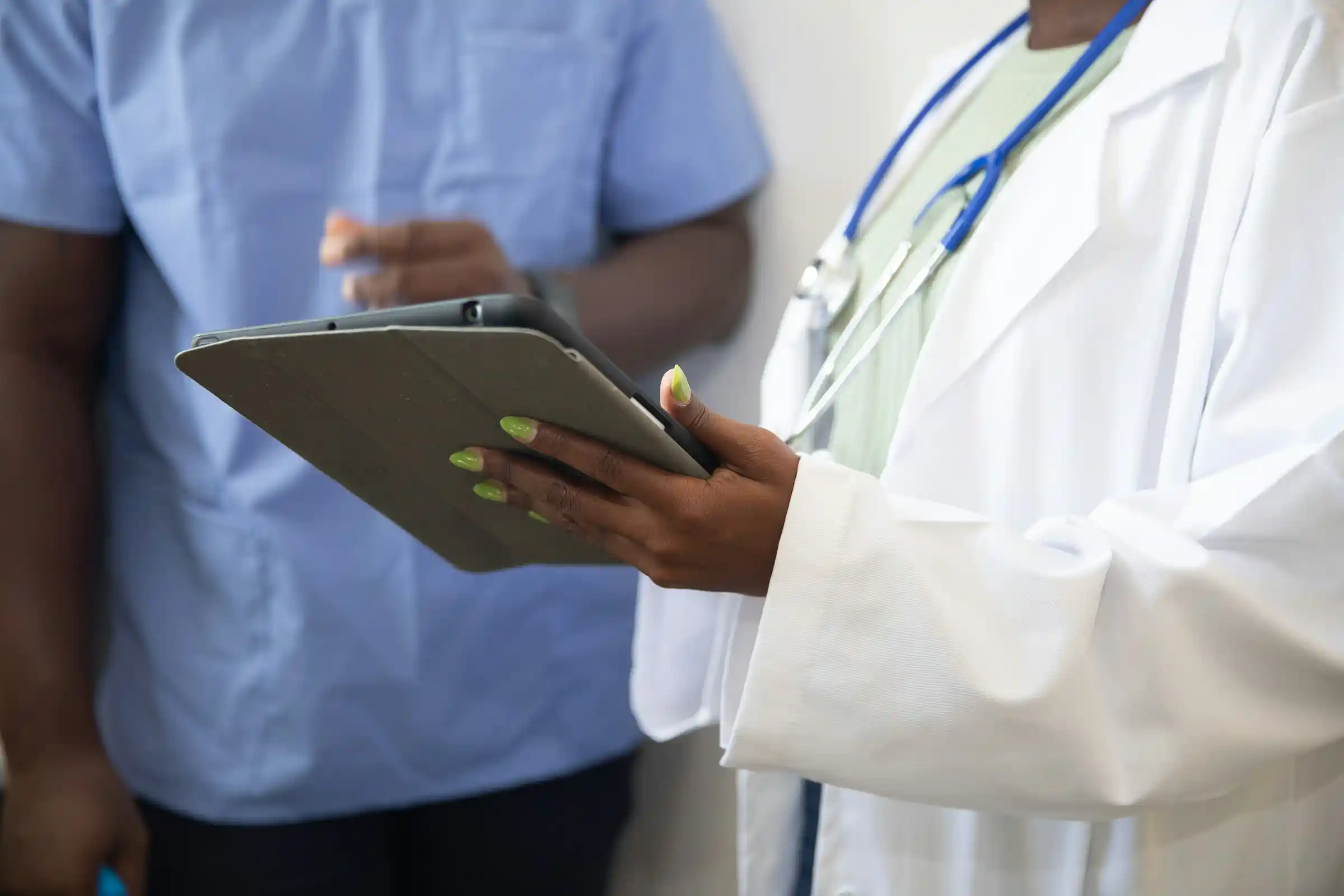 A doctor holding a tablet beside a colleague in scrubs