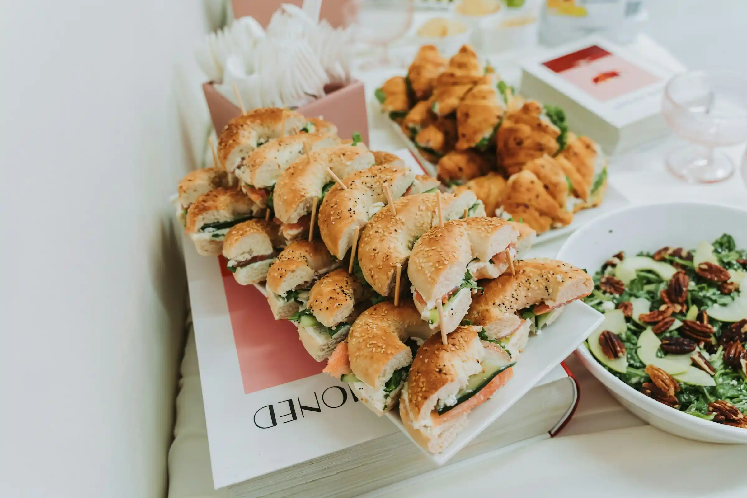 Tray of bagel and croissant sandwiches beside a green salad