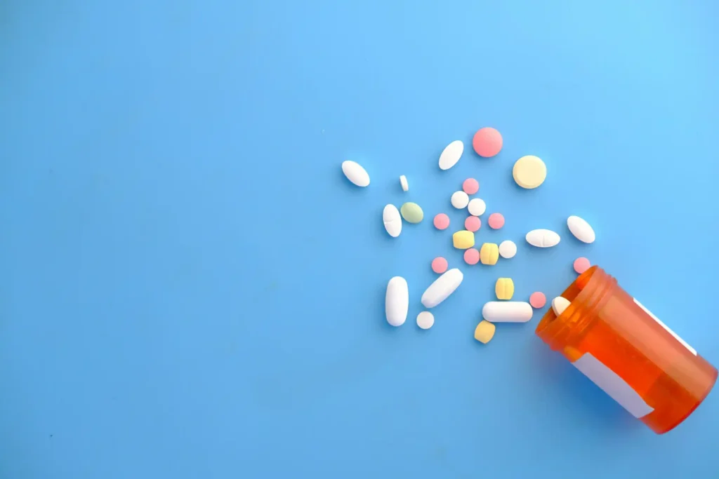 Assorted pills spilling from an orange prescription bottle onto a blue surface