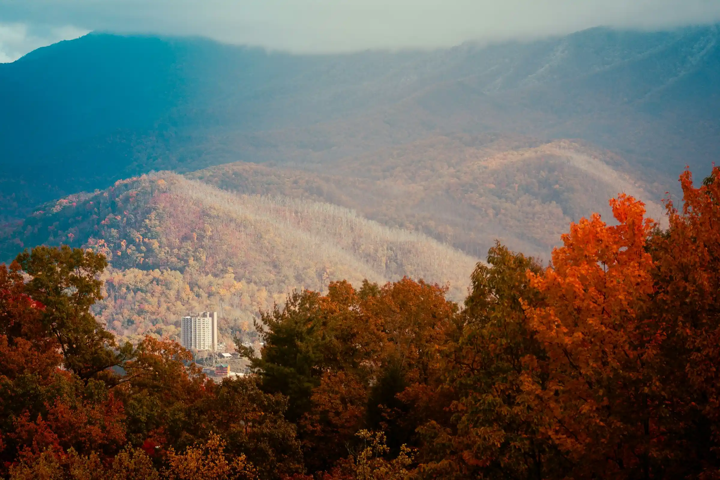 View from a mountain overlook showing Gatlinburg nestled among autumn-colored Smoky Mountain ridges