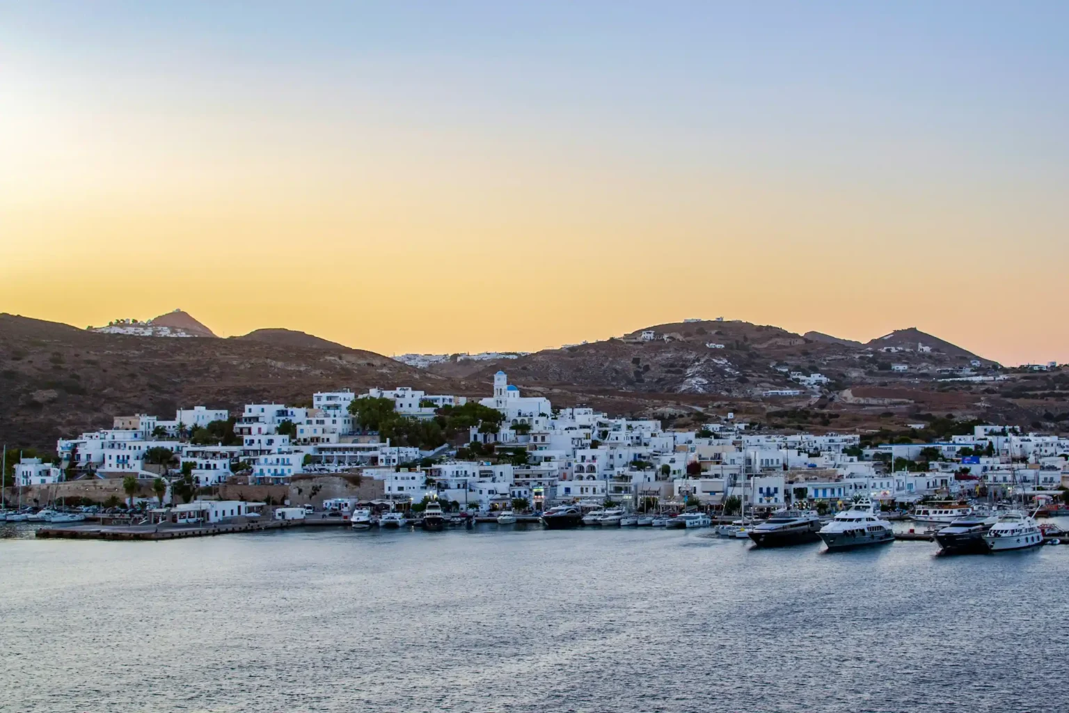 The whitewashed port town of Adamas at dusk with boats in the harbour, Milos