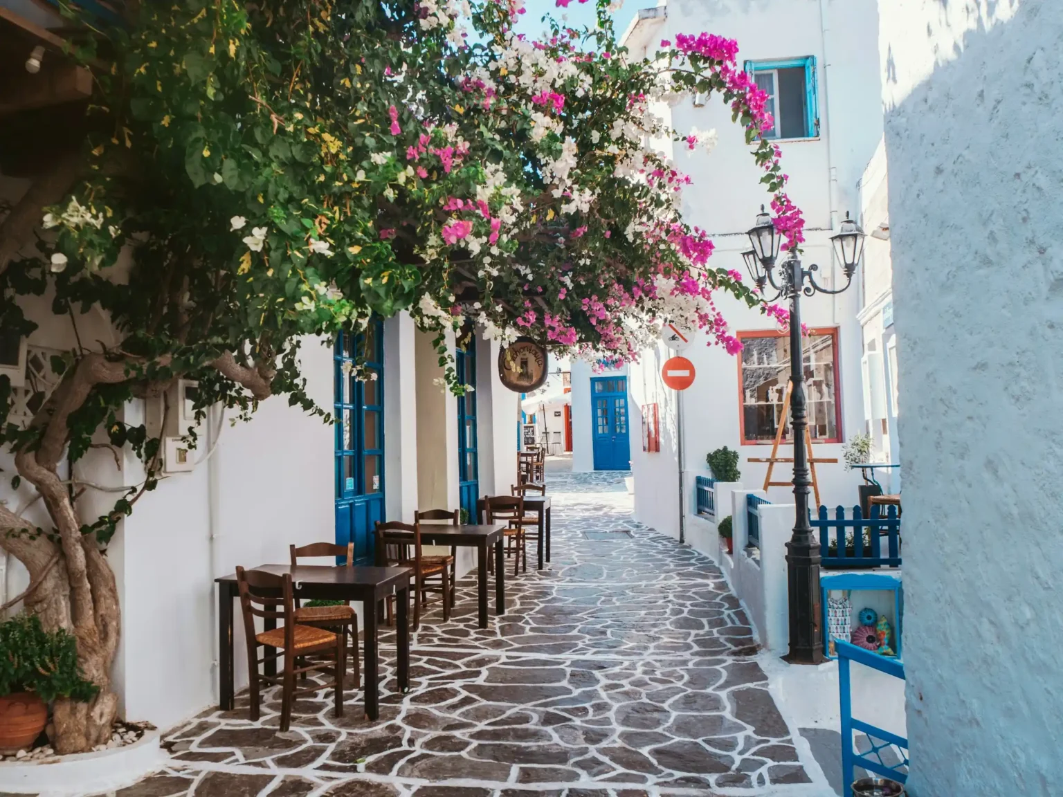 A whitewashed cobblestone alley with blue doors and bougainvillea in Plaka, Milos