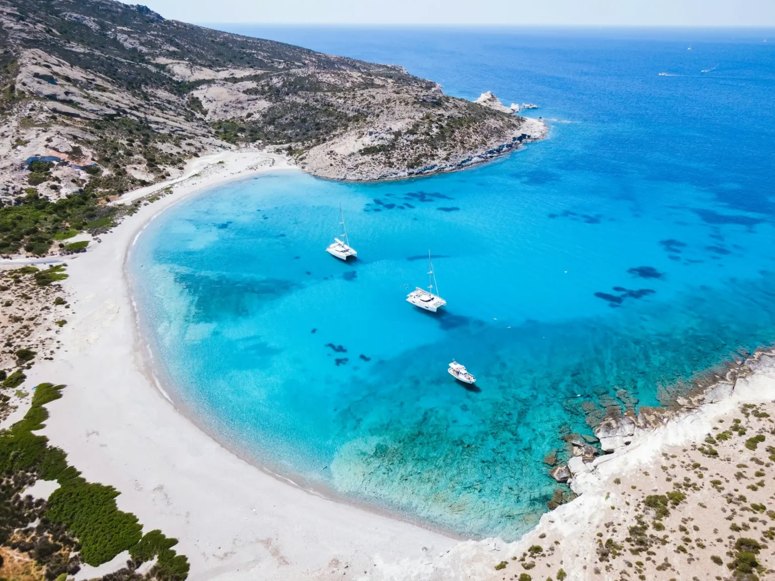 Sailboats anchored in a turquoise bay with a white sand beach, Milos