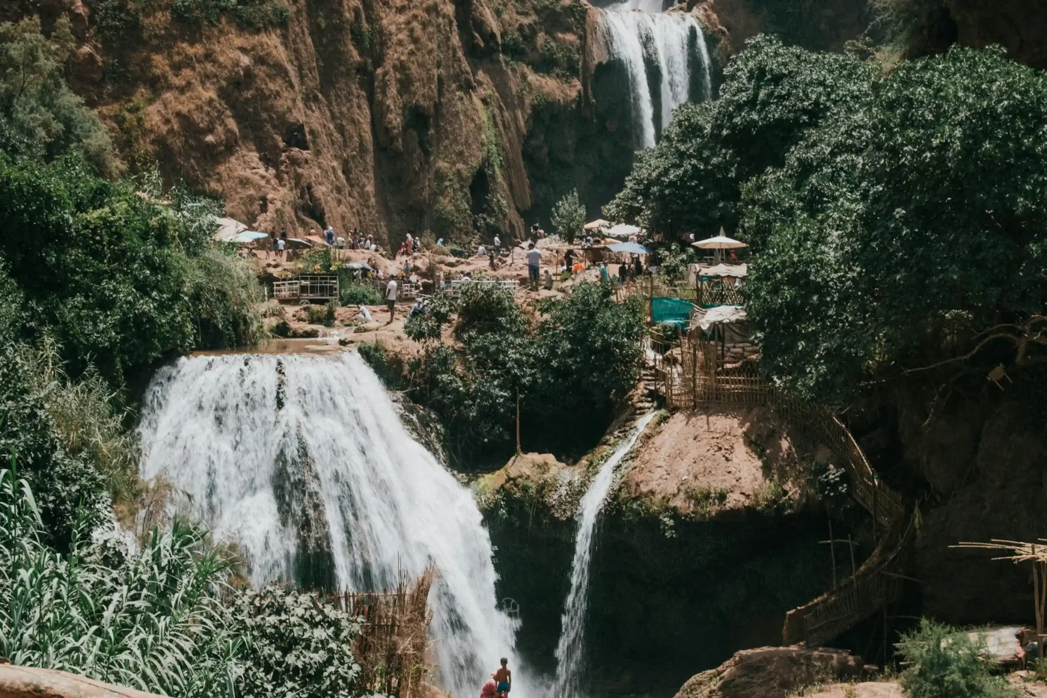 Ouzoud Falls cascading over red rock cliffs with green vegetation and a rainbow in the mist