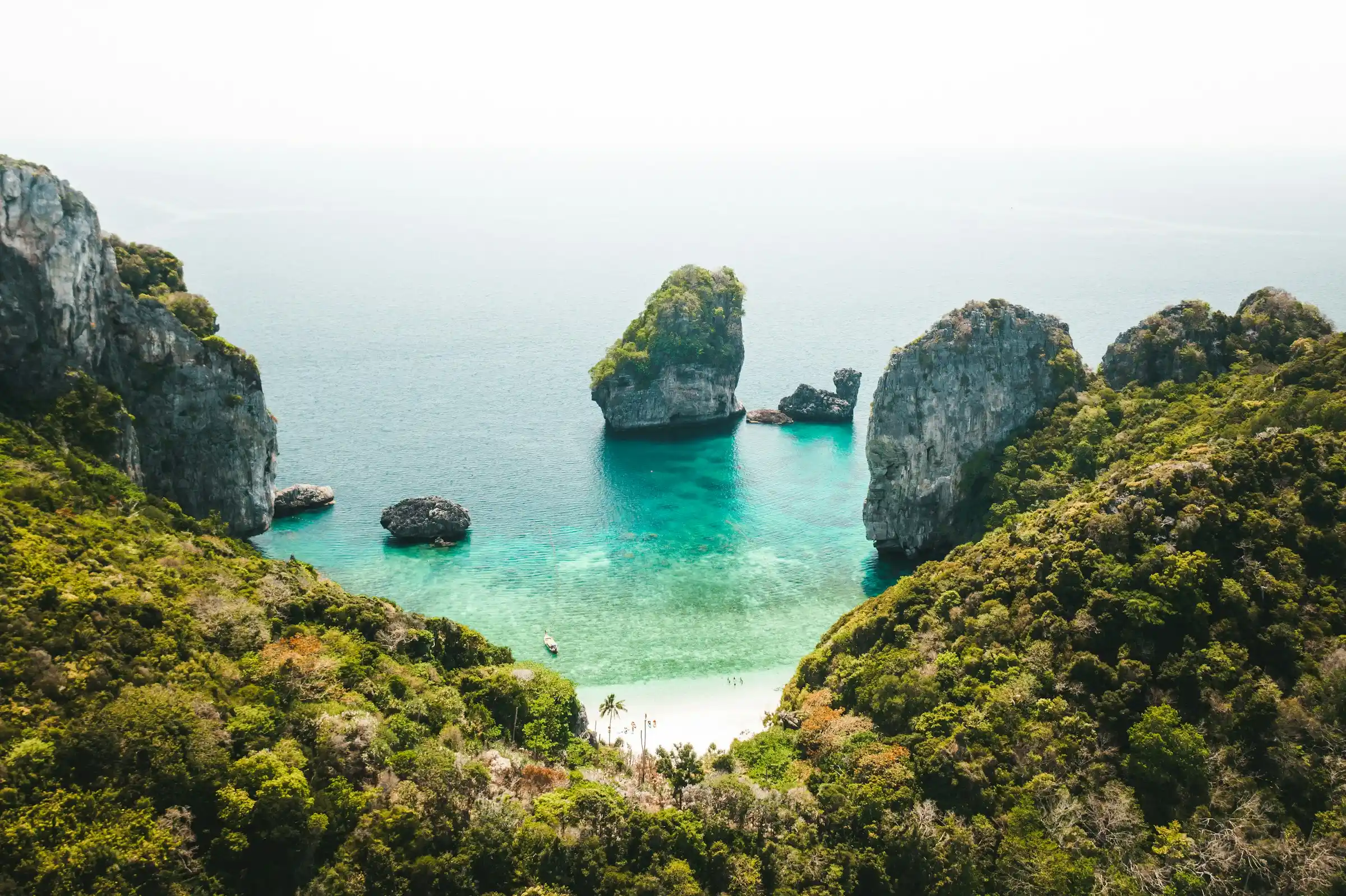 Hidden turquoise cove ringed by limestone cliffs with a longtail boat and a small beach at Phi Phi