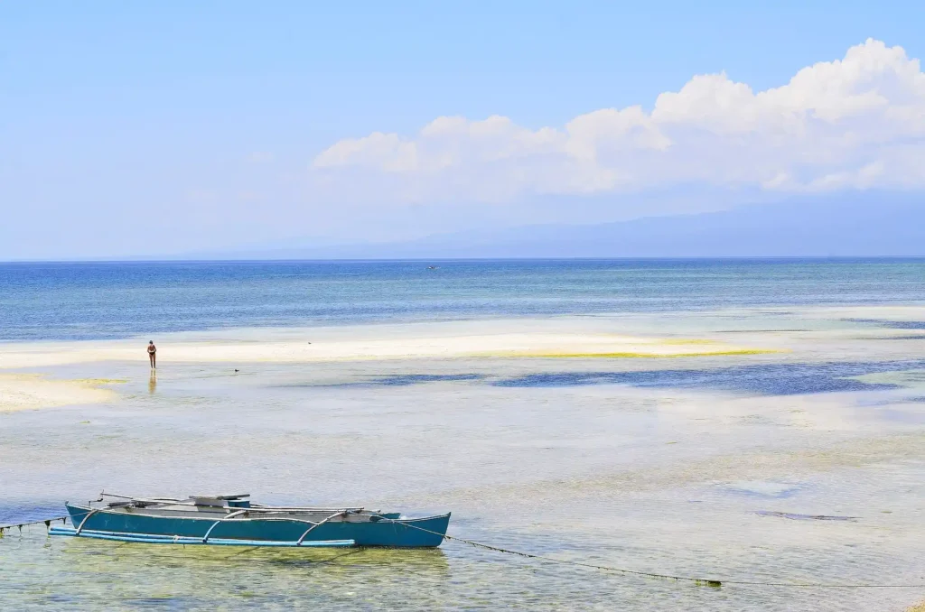 A traditional blue outrigger boat in the clear shallow water off the coast of Siquijor Island, Philippines