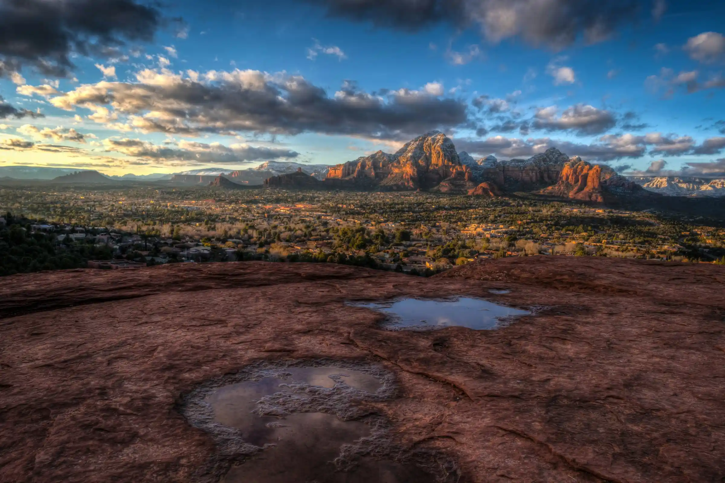 Golden-hour view of Sedona and its red rock formations from the Airport Mesa overlook, with rain pools on the slickrock