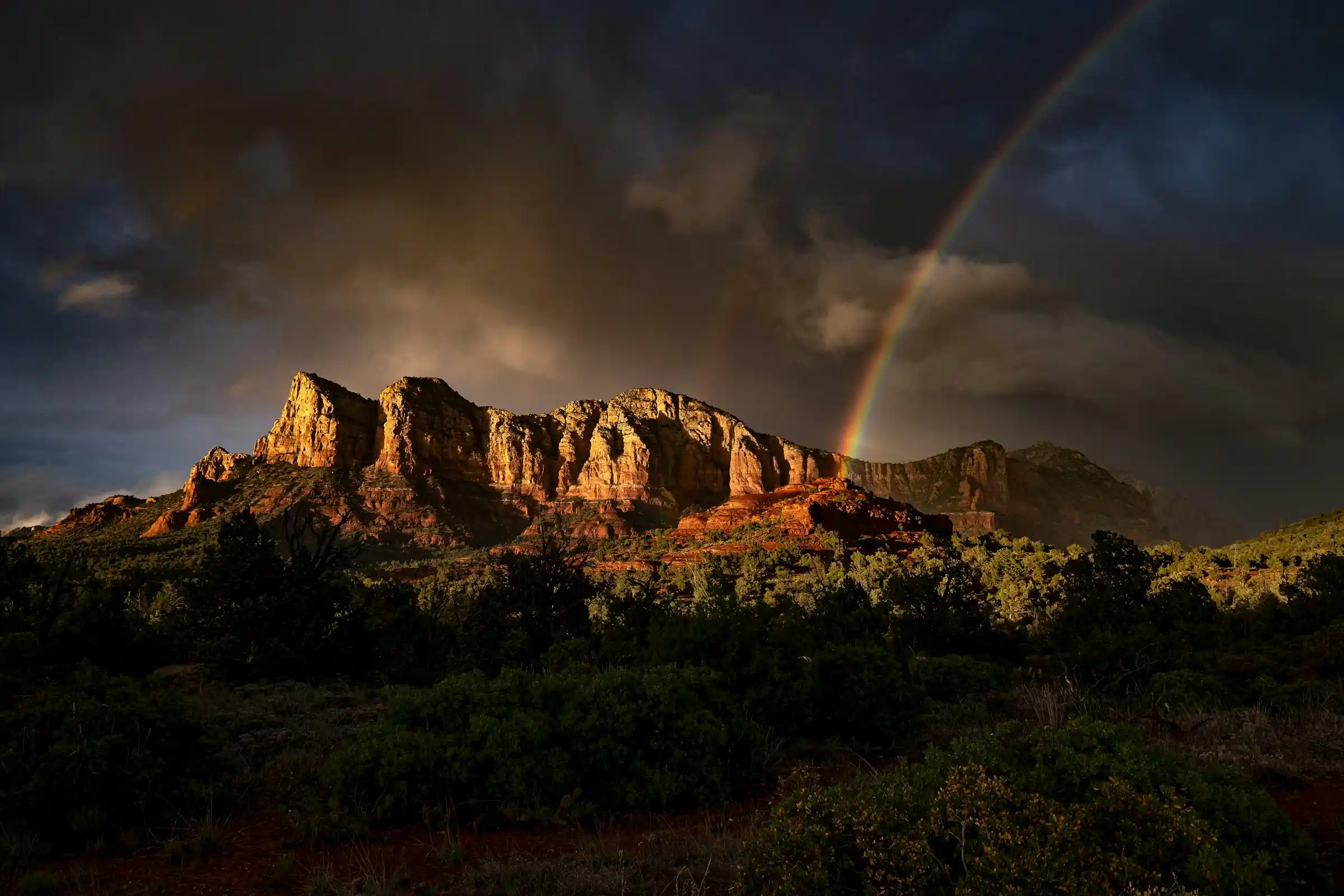 Rainbow arcing over a sunlit red rock ridge in Sedona after a monsoon storm