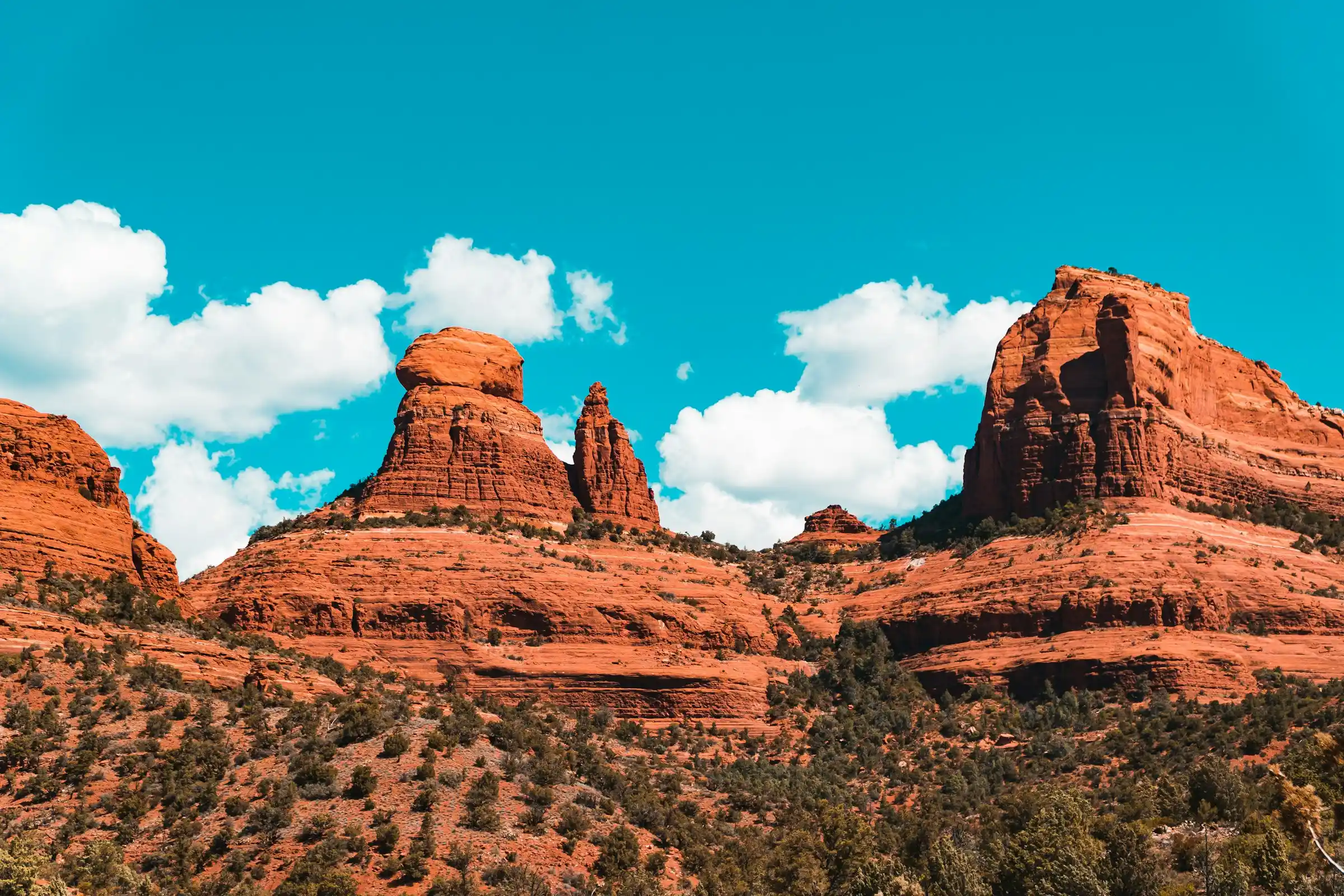 Red rock spires and buttes rising under a bright blue sky with white clouds in Sedona, Arizona