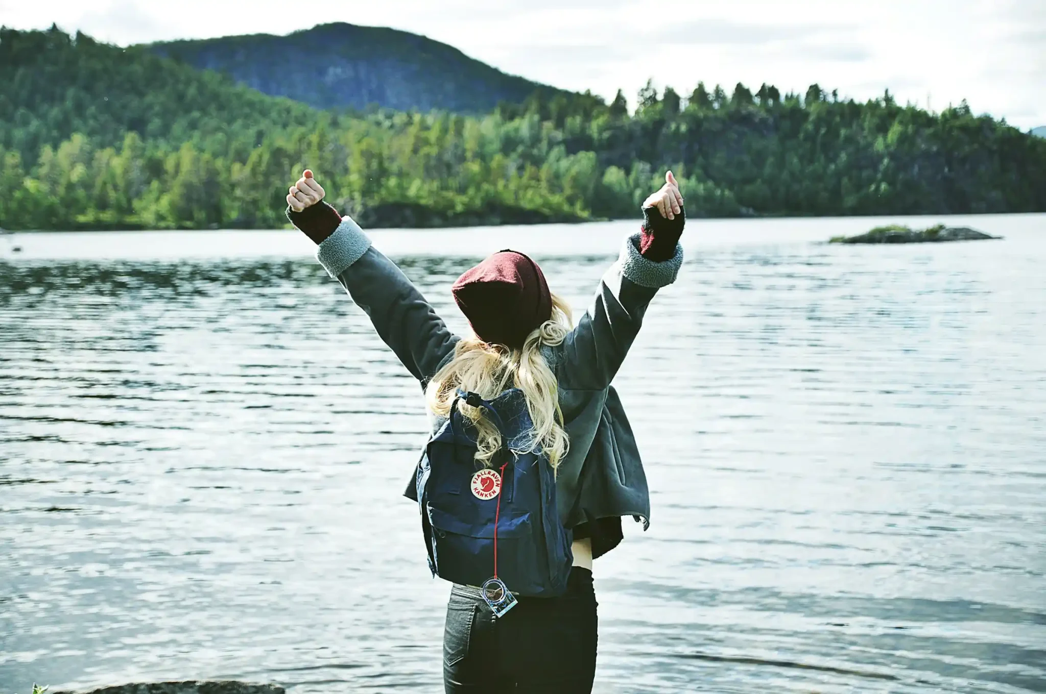Solo traveler with backpack celebrating by a mountain lake