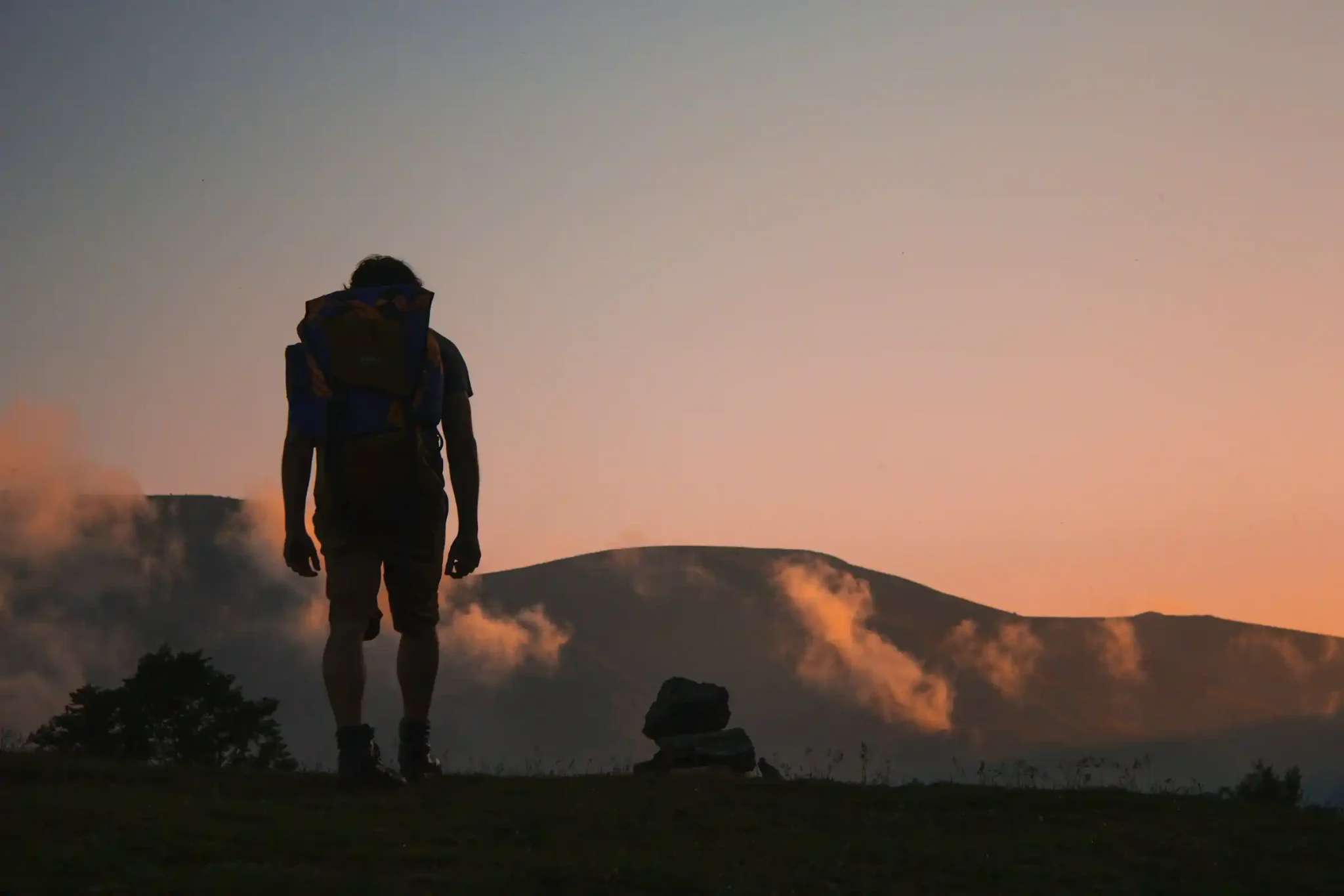 Solo hiker silhouette at sunset with mountains in the background