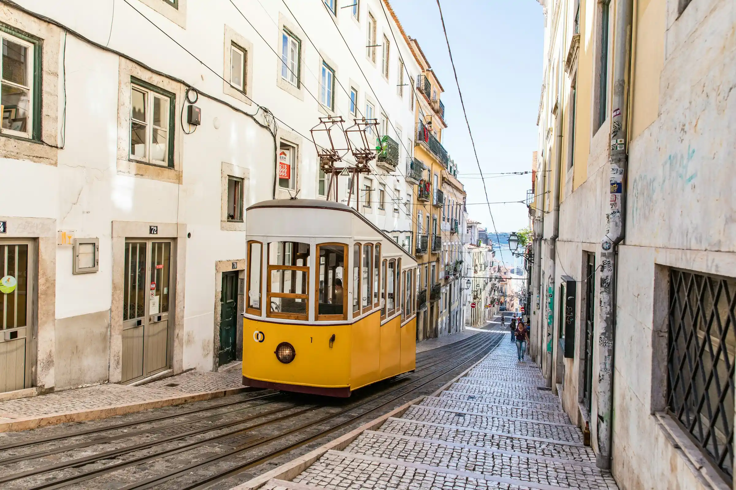 A yellow tram climbing a narrow tiled street in the Alfama district of Lisbon
