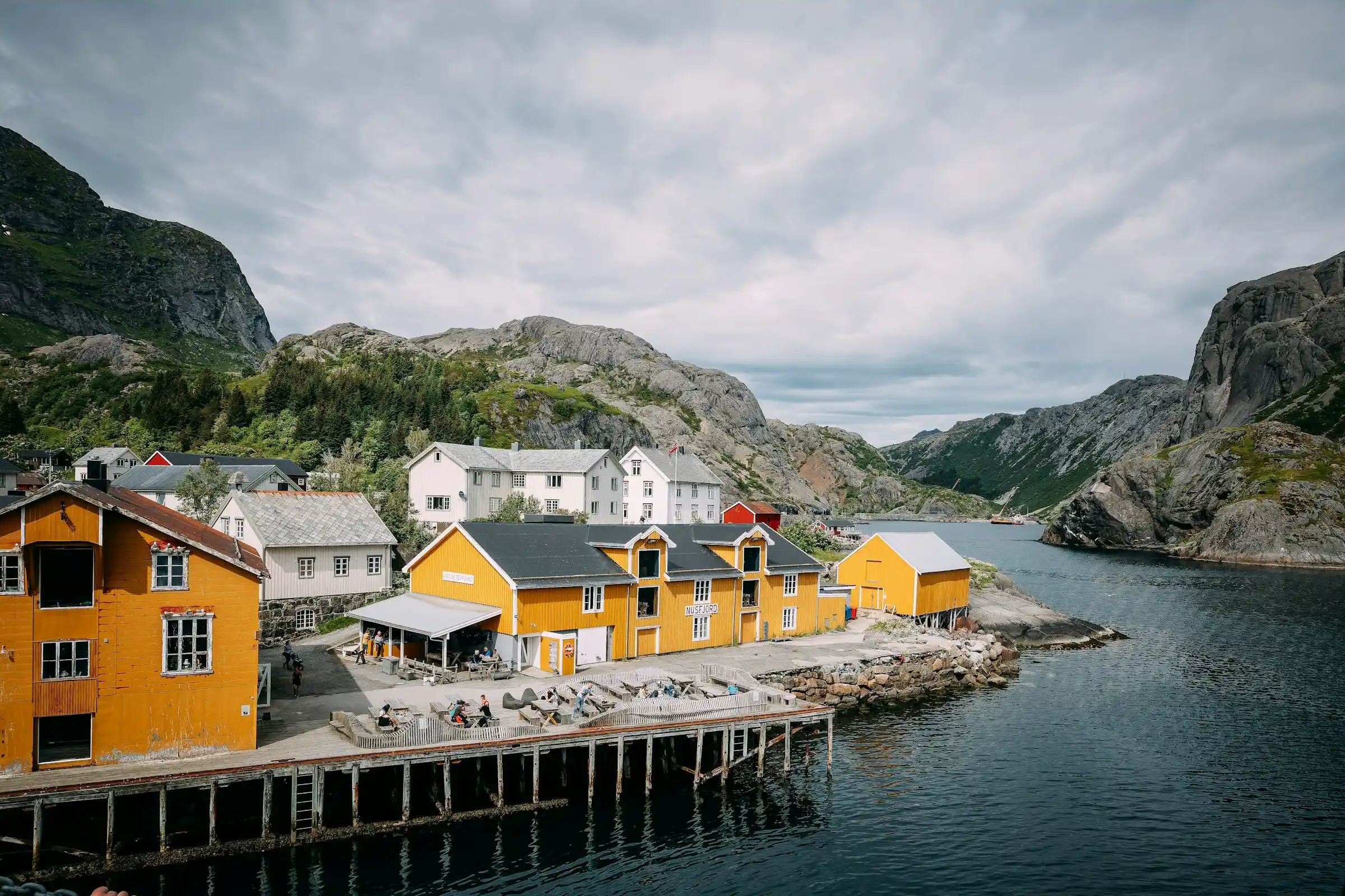 A deep blue Norwegian fjord winding between steep green cliffs with a waterfall