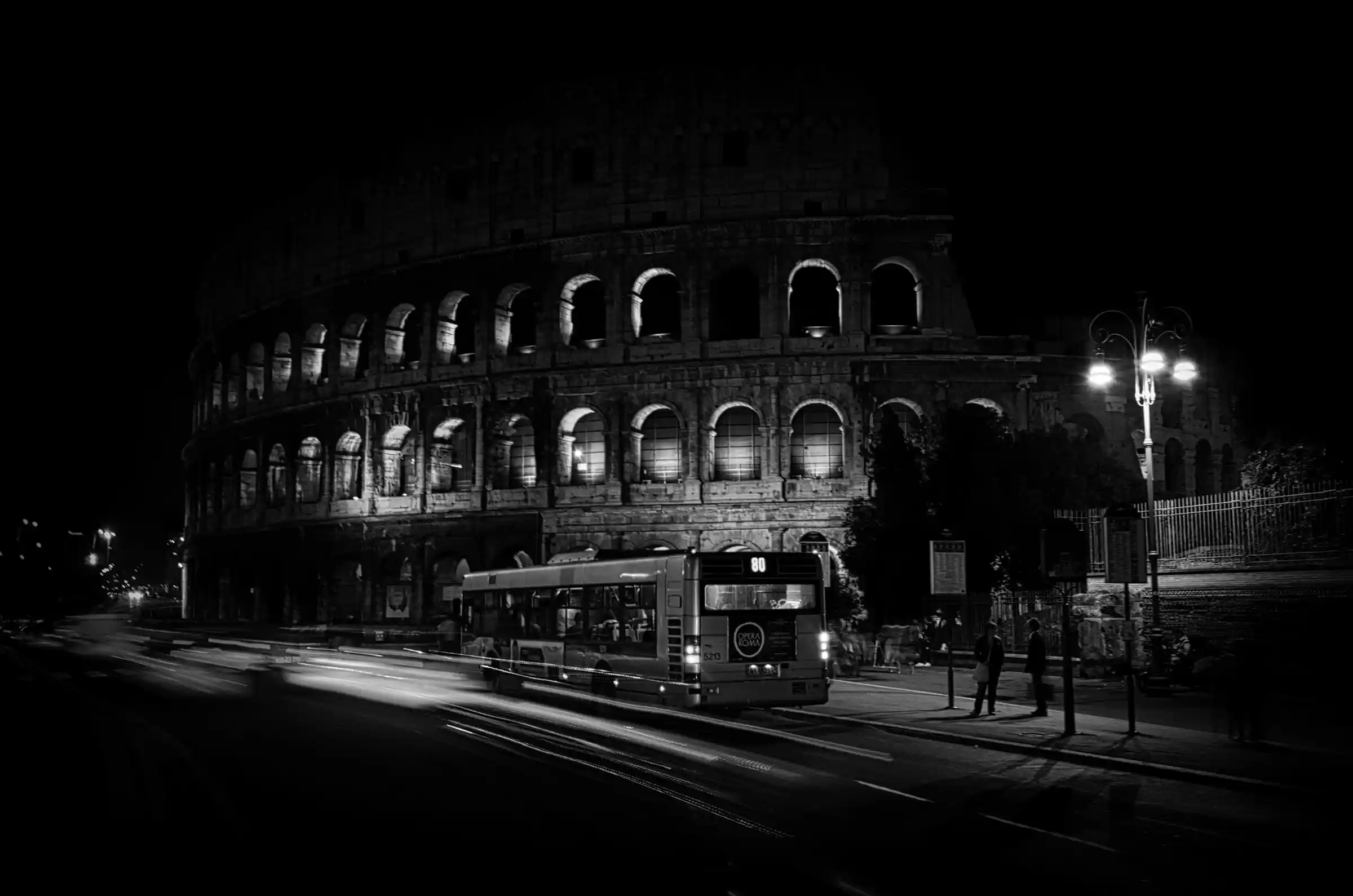 A red and grey ATAC bus passing ancient ruins in central Rome