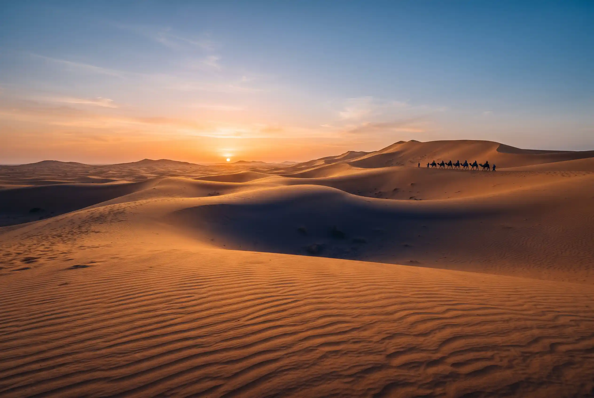 Golden Sahara sand dunes at sunset with long shadows and a distant camel caravan