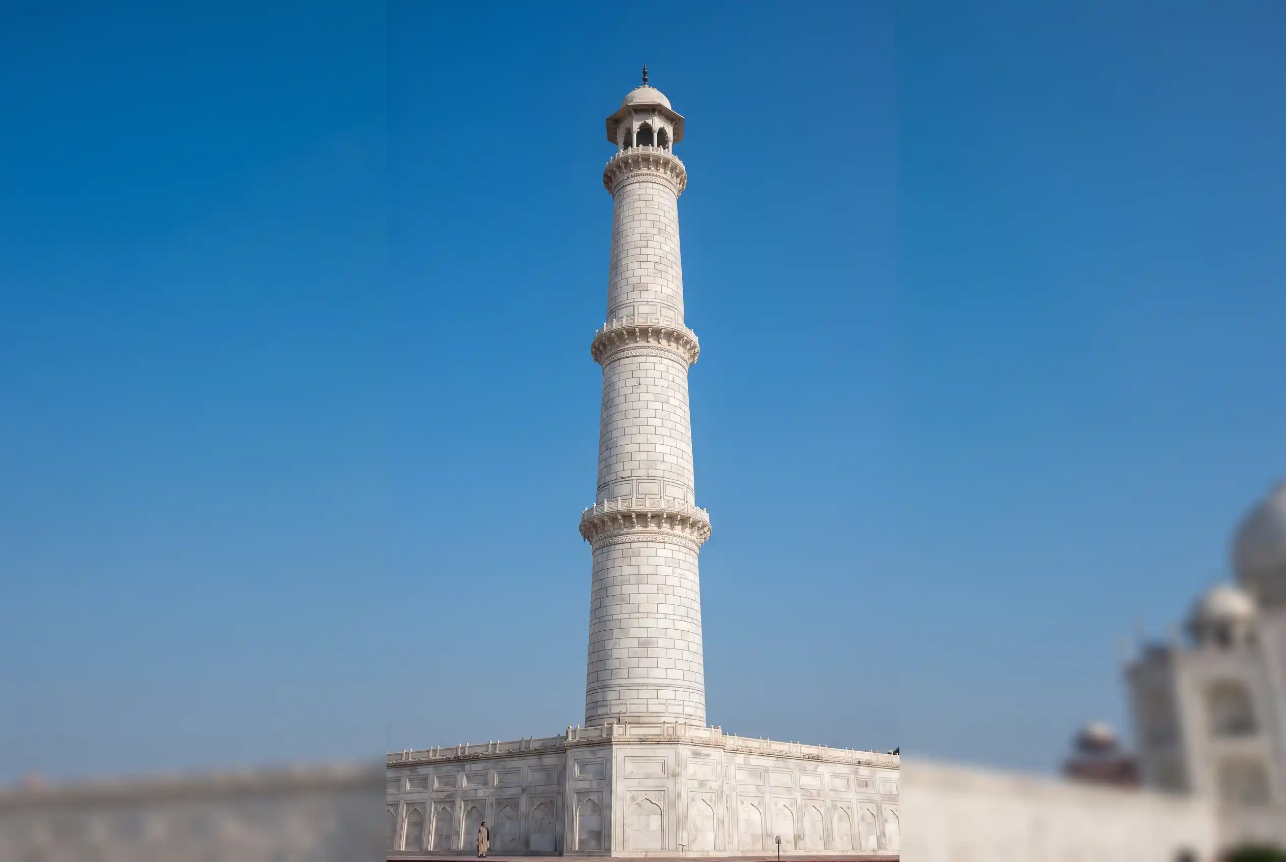 A white marble minaret of the Taj Mahal against a blue sky