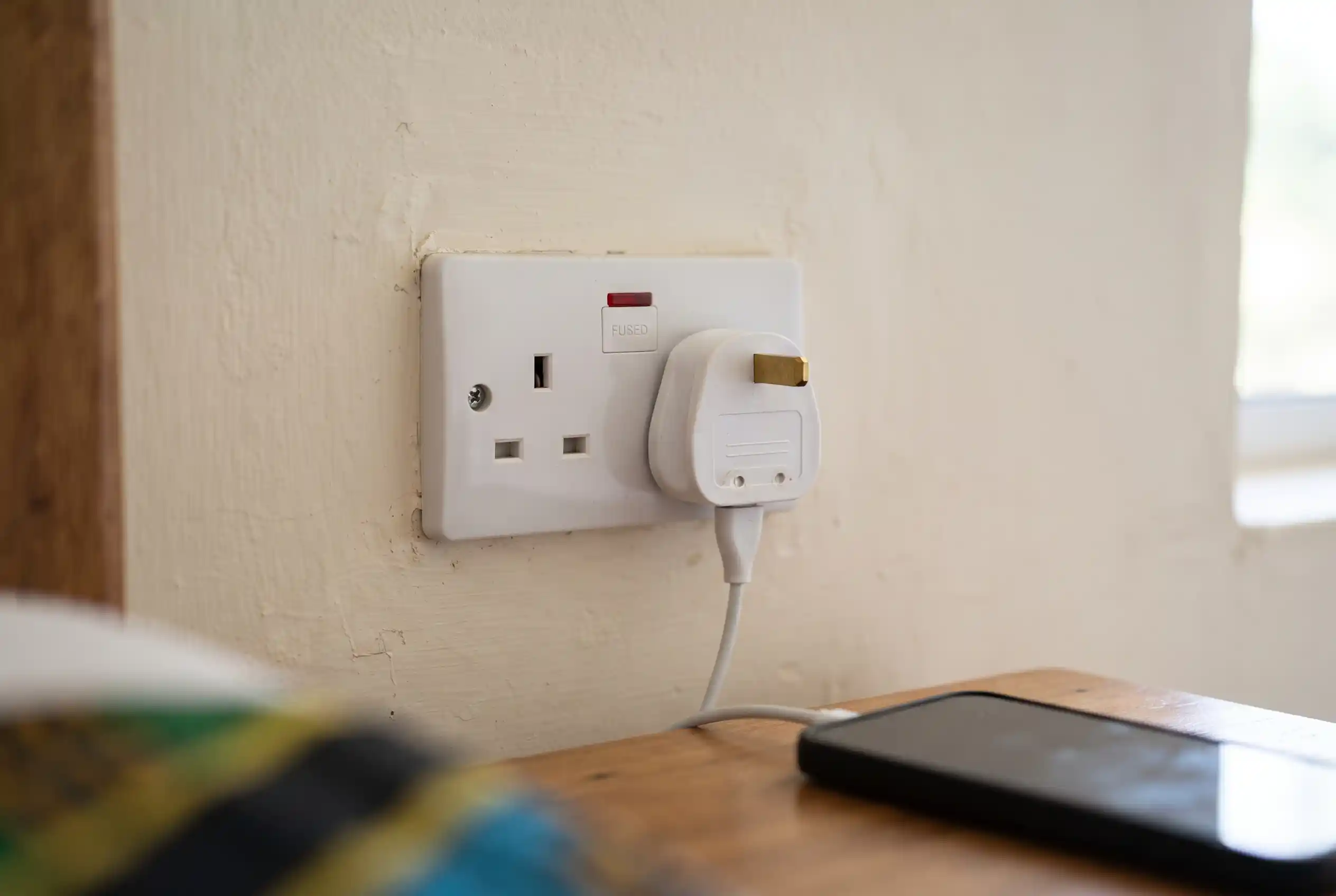 A UK style Type G wall socket in a Tanzanian hotel room with a charger plugged in