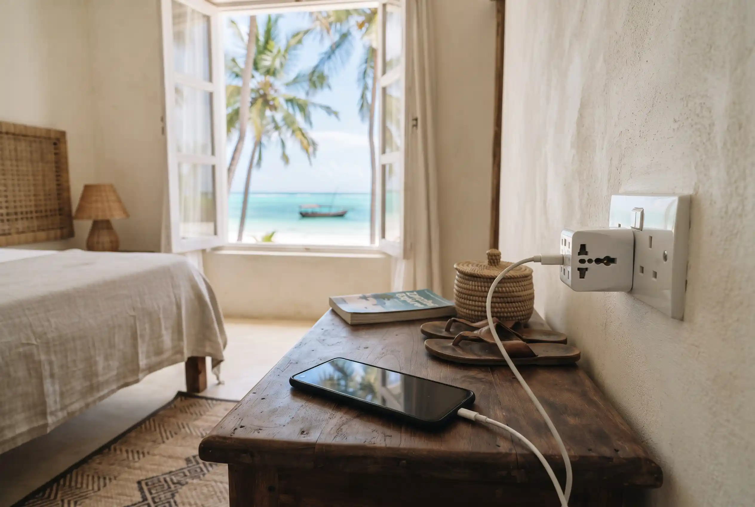 A phone charging through a travel adapter in a Zanzibar beach hotel room with sea view